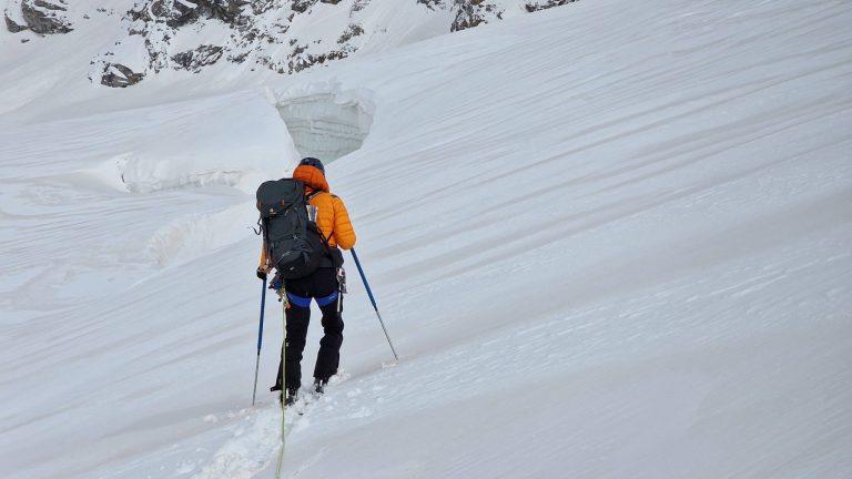 Skieur de randonnée en montée sur une large pente neigeuse
