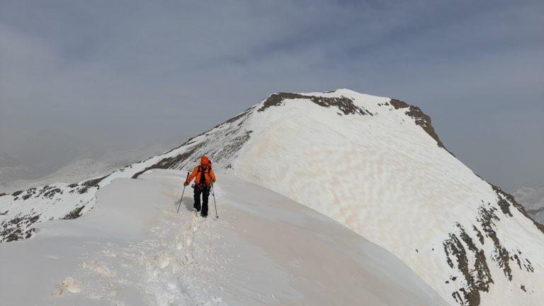 Skieur de randonnée sur l'arête enneigée, veste rouge