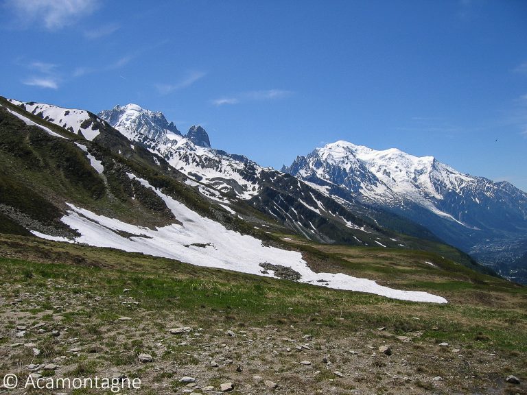 Le massif du Mont-Blanc enneigé vu depuis un alpage, névés et vallée en contrebas sous un ciel bleu