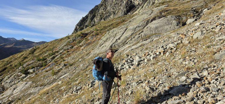 Randonneur sur le sentier de la montée, pentes d'herbe et de blocs au-dessus du Val Ferret