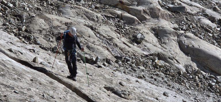 Randonneur casqué, bâtons en main, traversant la glace du reste de glacier