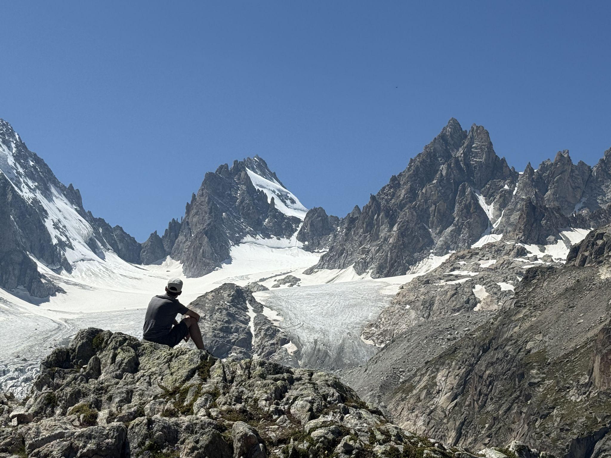 Randonneur assis sur un rocher, face au glacier de Saleina et aux sommets