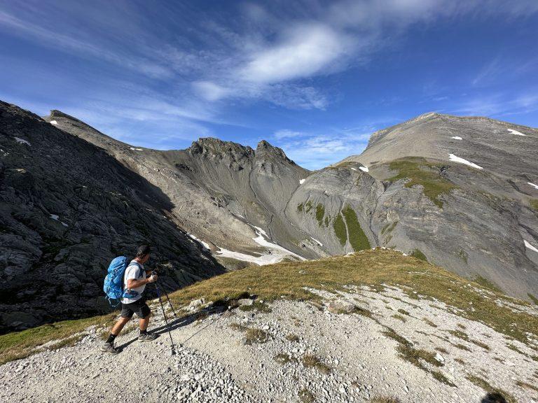 Randonneur sur une croupe herbeuse face aux crêtes qui dominent le Vieux Émosson