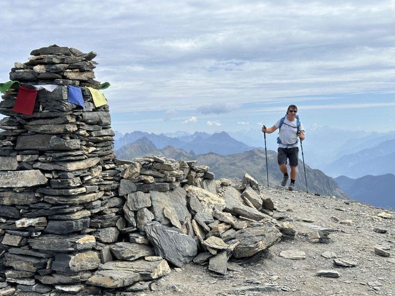 Grand cairn orné de drapeaux de prière au sommet du Cheval Blanc, un randonneur qui arrive
