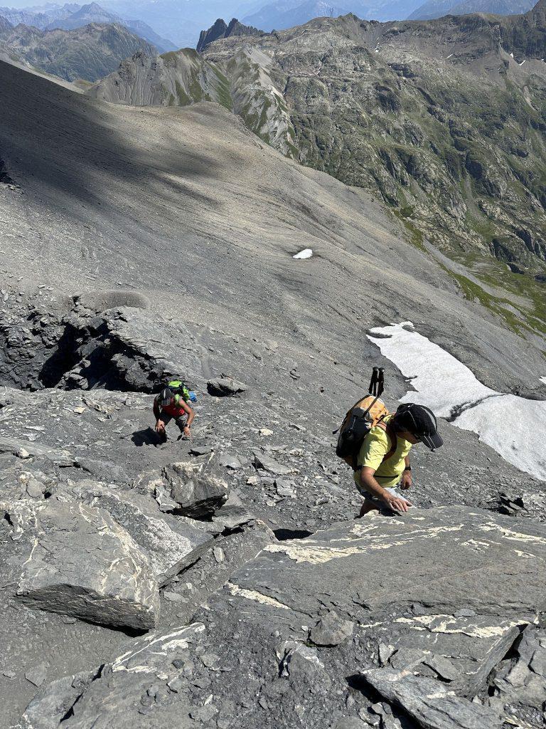 Randonneurs qui escaladent des dalles de schiste, un névé dans la pente