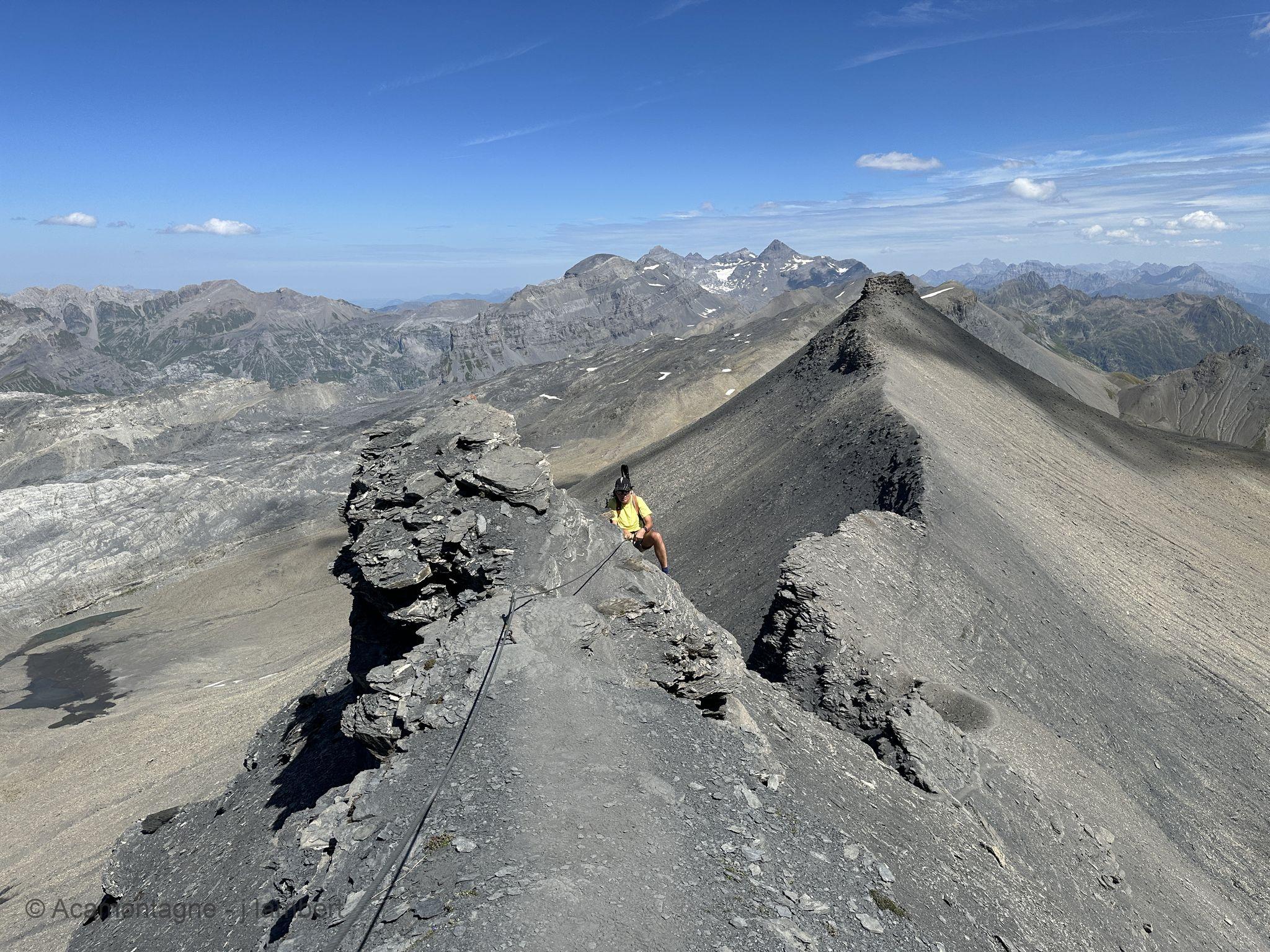 Randonneur sur une arête effilée équipée d'un câble, entre un gendarme et la pente