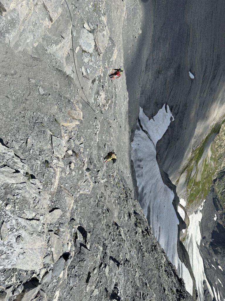 Vue plongeante sur deux randonneurs le long du câble, un névé dans le couloir