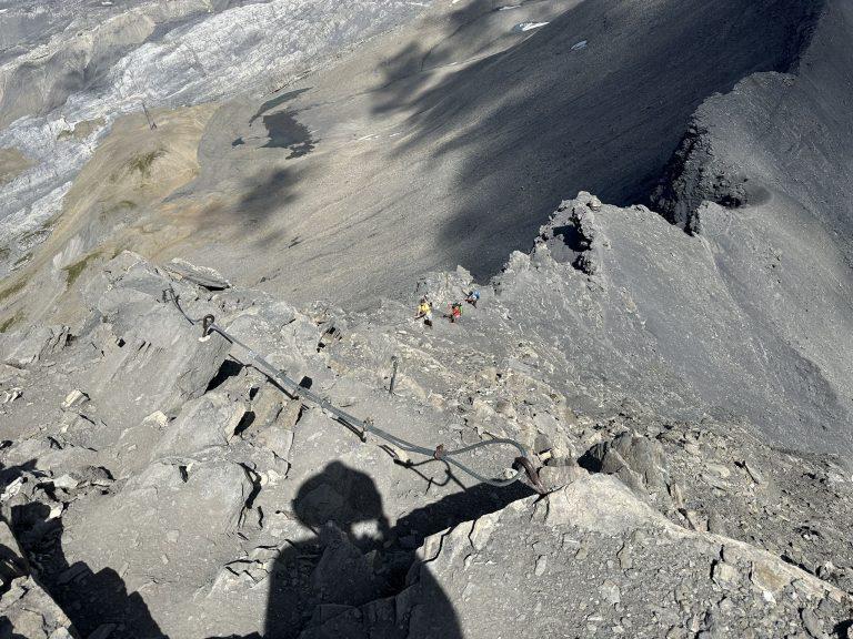 Ombre du photographe au-dessus du passage câblé, des randonneurs plus bas sur l'arête