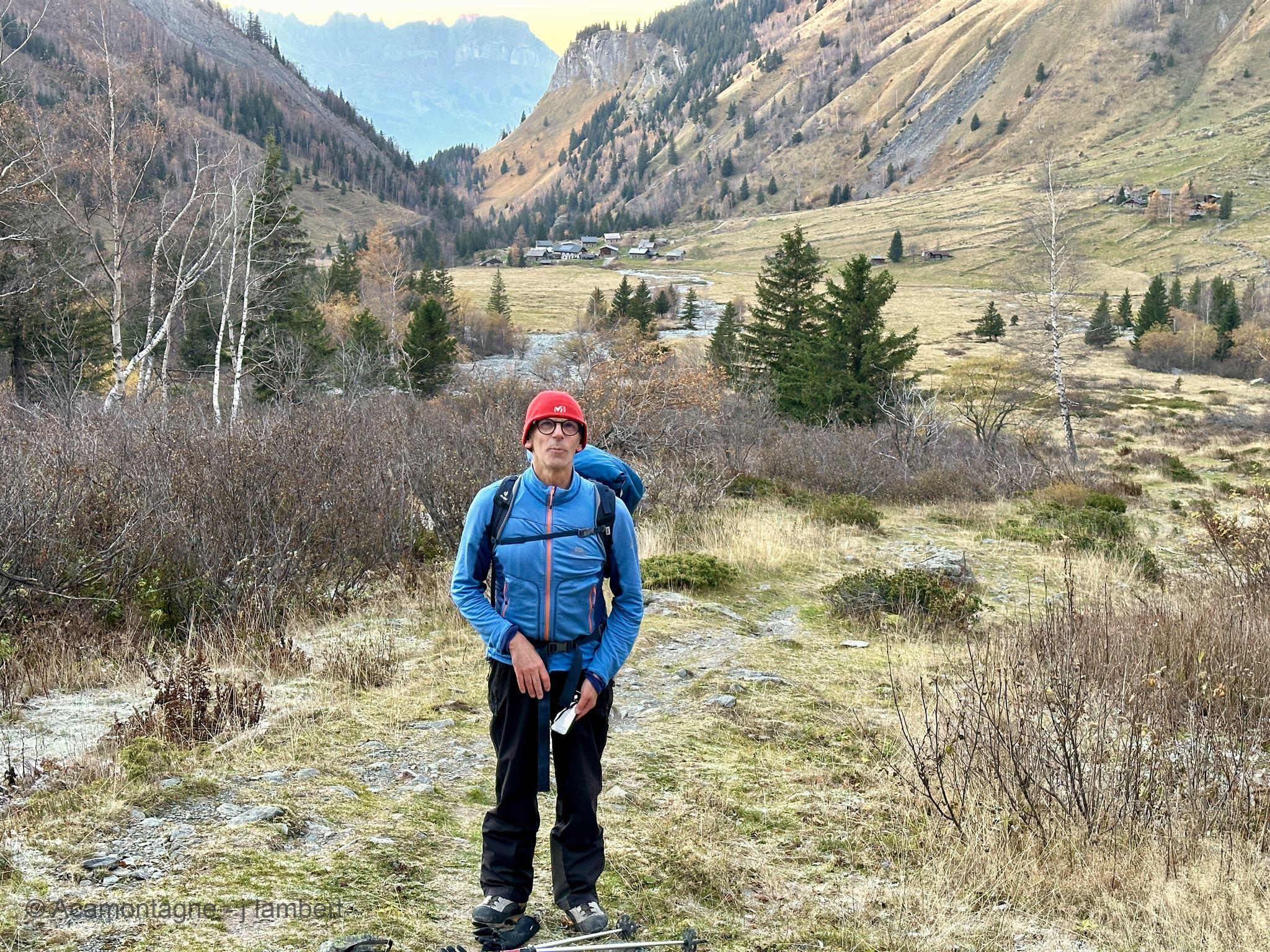 Randonneur au bonnet rouge dans le vallon de Miage, les chalets et les alpages derrière lui