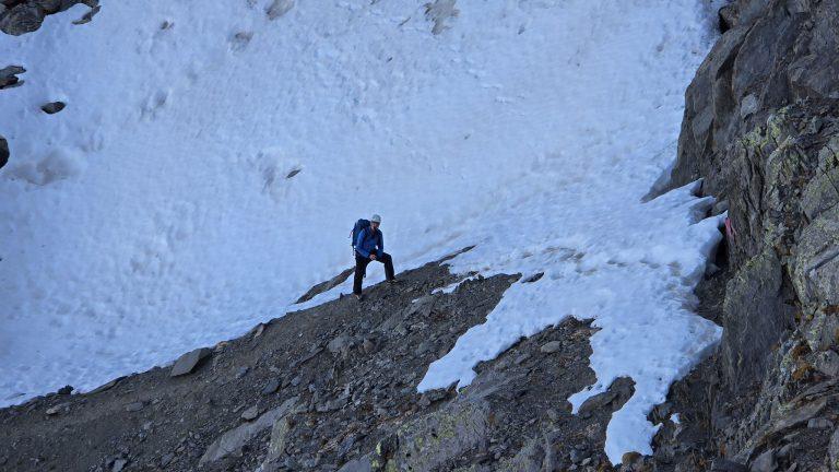 Randonneur casqué traversant une pente de neige au pied des rochers
