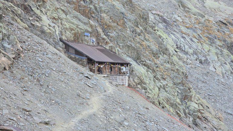 Le refuge de Plan Glacier accroché à la pente d'éboulis, le sentier en lacets à ses pieds