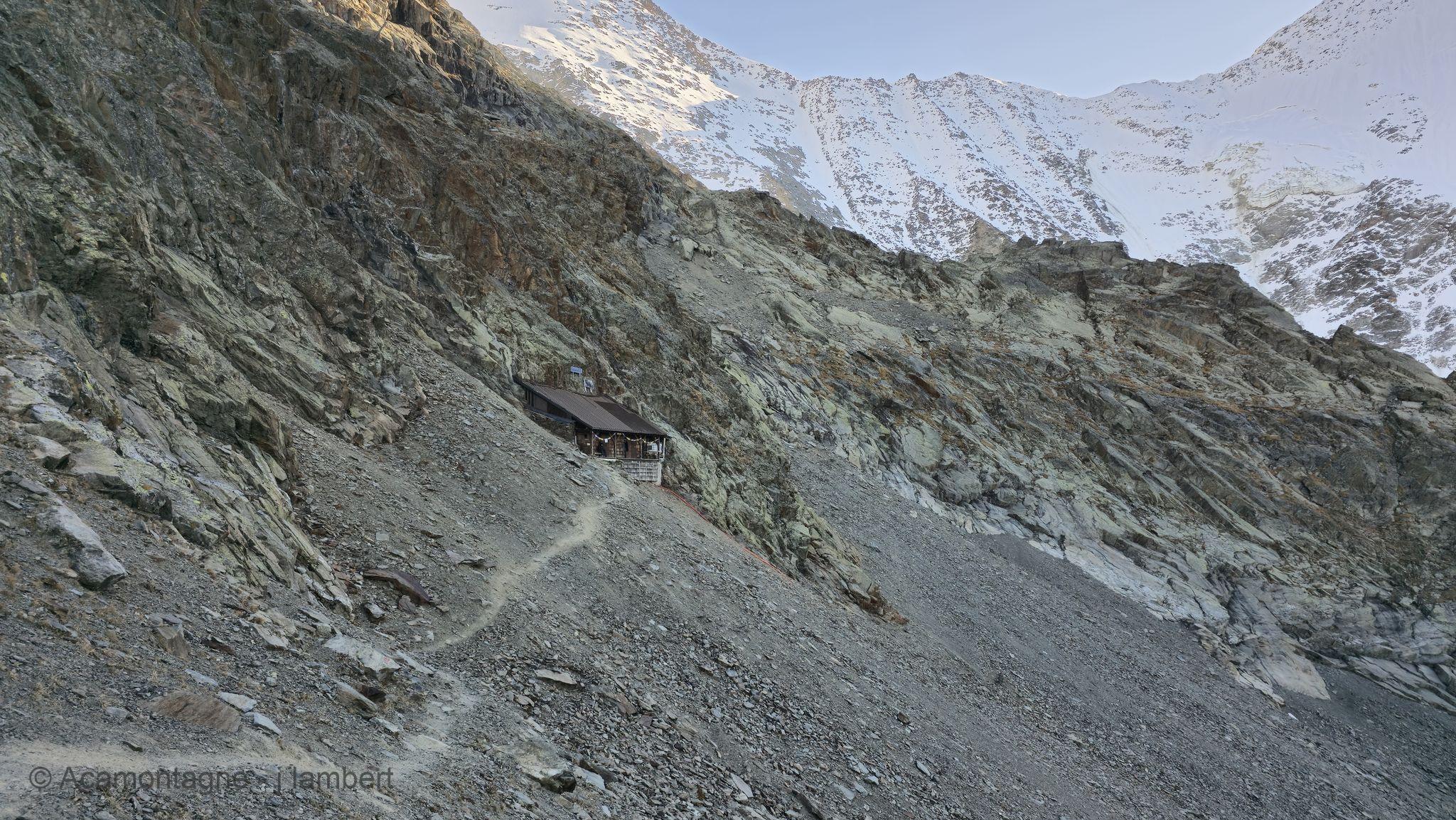 Le refuge de Plan Glacier, minuscule au pied de la paroi, sous les faces enneigées