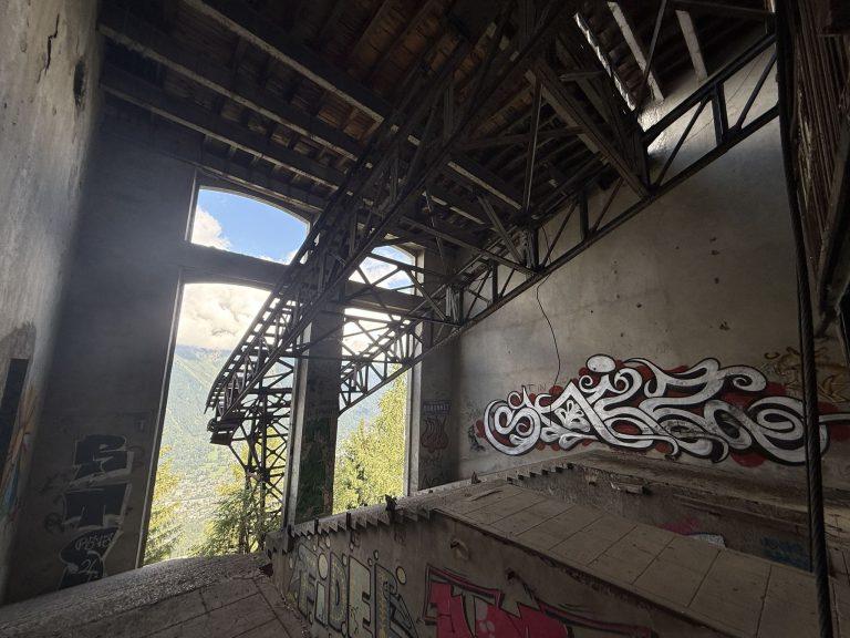 Intérieur de la gare de La Para : charpente métallique de l'ancien téléphérique des Glaciers et murs tagués, la forêt derrière les grandes baies