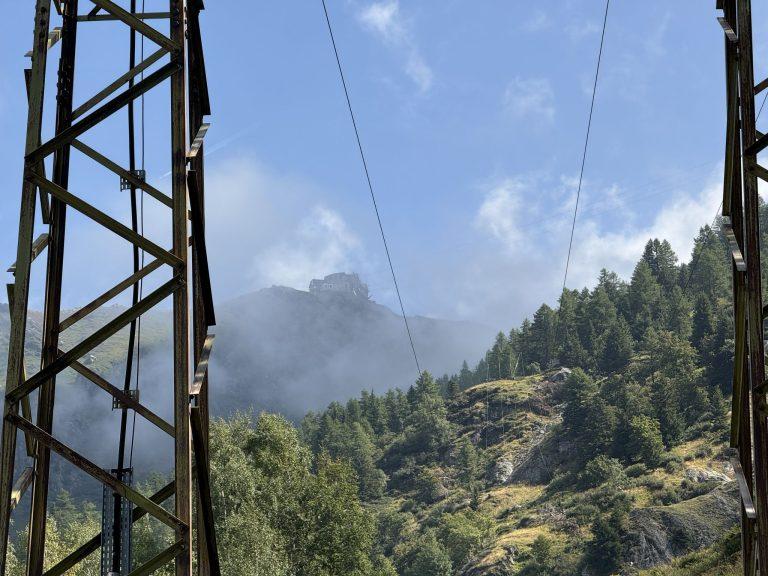 Entre les montants d'un pylône, les câbles de l'ancienne ligne électrique, encore en activité, montent vers la montagne dans la brume