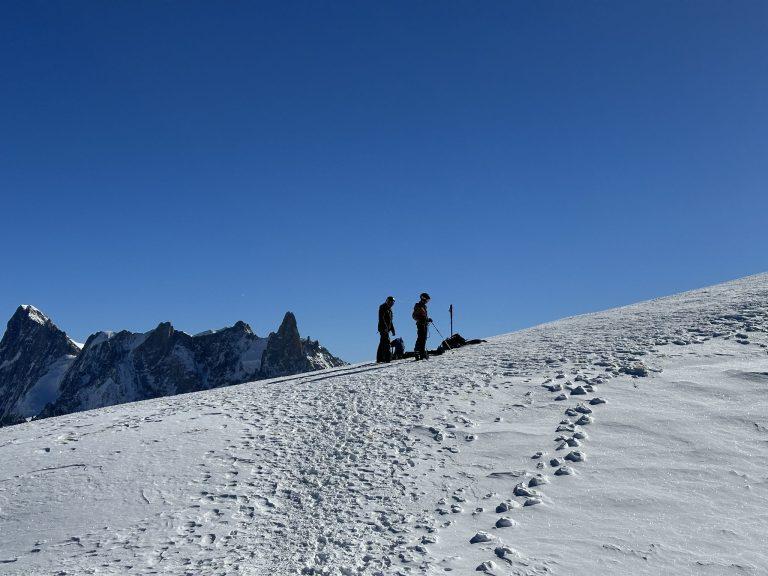 Deux skieurs se préparent au pied de l'arête, des traces de pas dans la neige