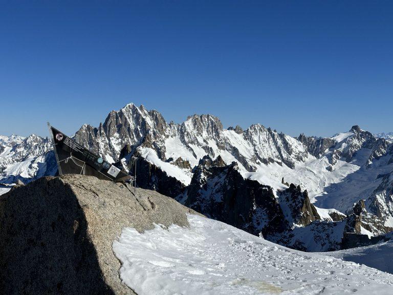 Un rocher et un panneau au premier plan, les sommets enneigés de l'autre côté de la vallée