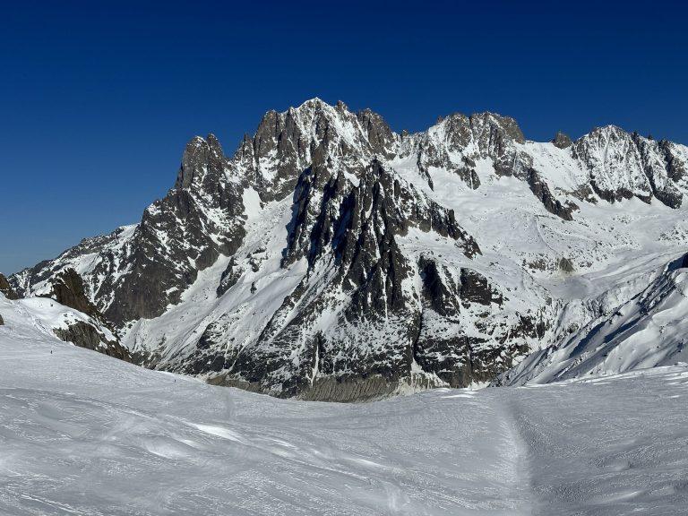Grand massif rocheux et enneigé dominant le glacier, sous un ciel bleu profond