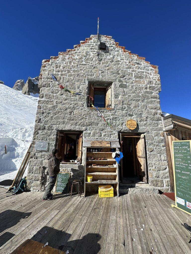 Façade en pierre du refuge du Requin, sa terrasse en bois et son ardoise des menus