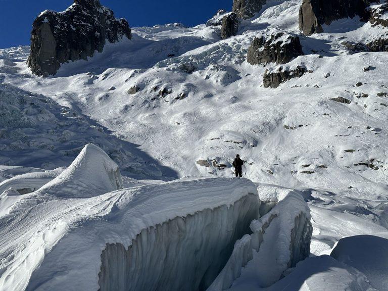 Un skieur au bord d'une grande crevasse, sous des rochers sombres